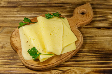 Slices of cheese on cutting board on wooden table