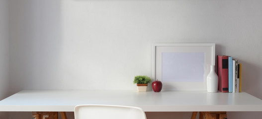 Minimal workspace with copy space and mock up frame with books on white table and white wall