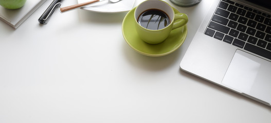 Top view of modern workplace with laptop computer and green coffee cup on white table