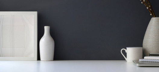 Modern workspace with mock up frame and ceramic vase on white table and grey wall background