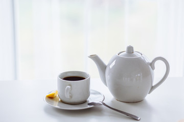 white cuo and white teapot on the white table with black tea and fresh lemon