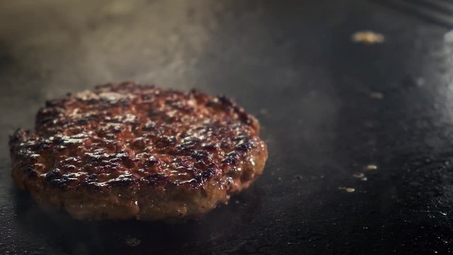 Slow motion extra close-up of a cook Flips and throws a burger cutlet. The kitchen in the restaurant fries meat on an electric stove grill