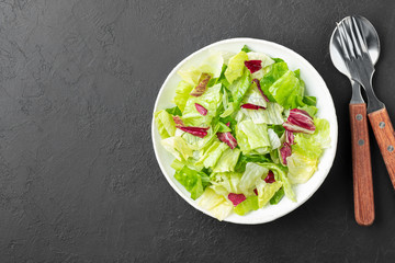 Vegetable fresh mixed salad with red and green lettuce on black slate background. Healthy food. Flat lay. copy space.