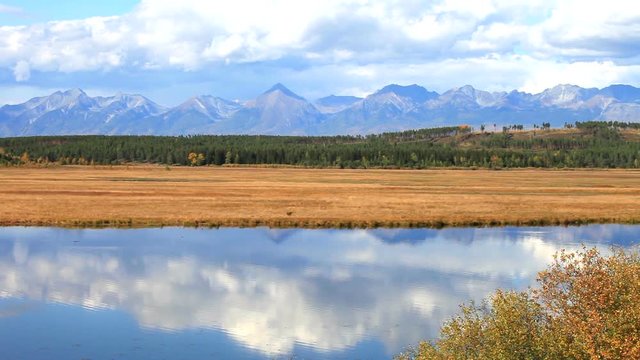Beautiful autumnal landscape with reflection in the River of blue sky with fast flying clouds. Siberia, Buryatia, Tunka Valley. Natural autumn background, time lapse 