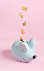blue piggy bank in the form of a mouse with falling coins on a pink background