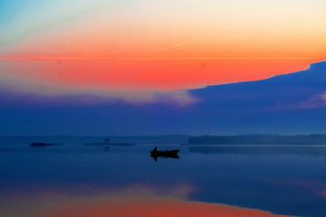 Fototapeta na wymiar fisherman in a boat, dawn over the lake