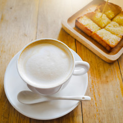 Coffee cup and butter toast on wooden table with warm sunlight morning (soft focus at cream bubbles)