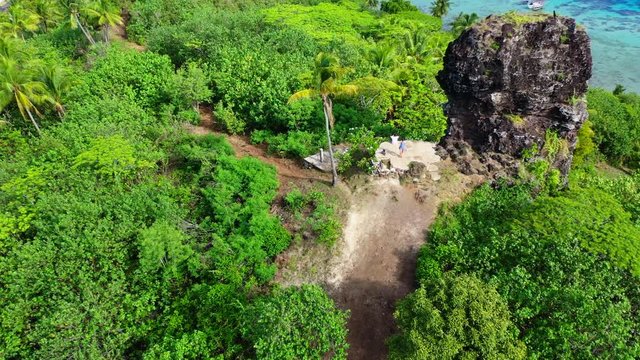 Aerial shot from the back of a young couple next to a ruin wall on a beautiful tropical island, drone flying forward while tilting down - Bora Bora, French Polynesia