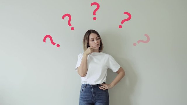 Young beautiful girl having questions. Charming girl thinks. Portrait of a thinking pretty girl. Question marks over the head girl.