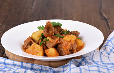 Beef stew with potatoes in a white plate.