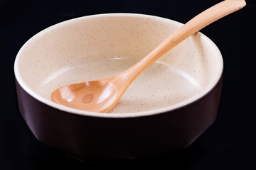 Wooden spoon and ceramic bowl on black blackground