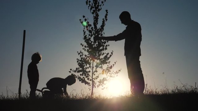 happy family of farmers a silhouette concept slow motion video. dad son and daughter children lifestyle plant and water the tree outdoors in the park. happy family little girl and boy works in garden