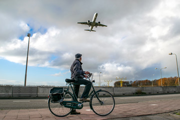 Gentleman on bike watches a jet aircraft soar overhead moments before landing at Amsterdam's...