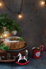 Homemade Christmas cake decorated with sugar powder and spruce twigs with christmas decorations and garland on dark background. Copy space