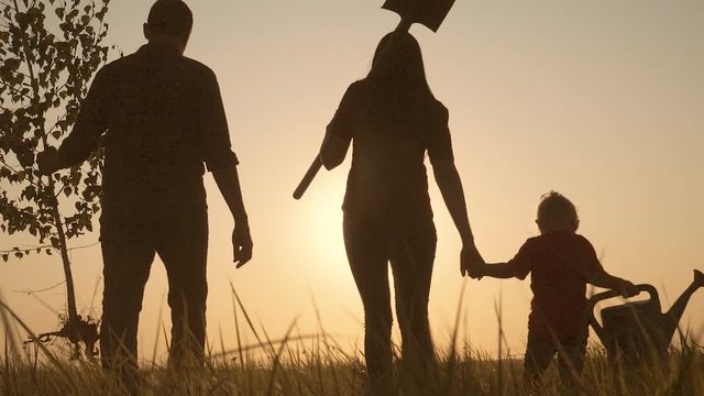 lifestyle happy family walking agriculture of farmers a silhouette concept slow motion video. mom dad son and daughter walk go children plant and water the tree outdoors in the park. happy family