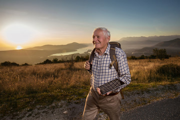 Happy old man just reaches the top of hill.Handsome senior man hiking, exploring, holding digital tablet.