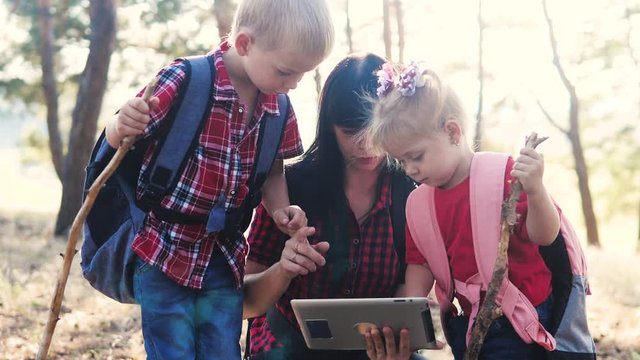 happy family little boy and girl scout navigation tourists teamwork slow motion video concept. mom son and daughter hiking in the forest looking for a way on a digital tablet. group of people hikers