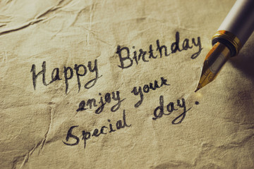 Happy birthday enjoy your special day. Vintage brass pen writing birthday greetings on old paper.