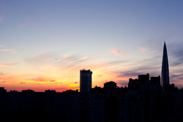 Dark silhouettes of urban buildings, houses and skyscrapers on background of colorful sunset with cirrus clouds, St. Petersburg, Russia