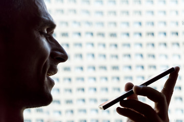 Close up of a young Caucasian man holding and talking on a smartphone in his room