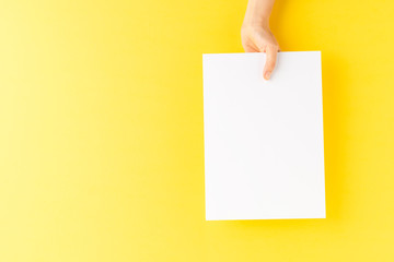 Overhead shot of female hand holding empty paper sheet on yellow background