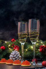 New Year and Merry Christmas concept. 2 glasses of champagne, tartlets with red caviar, spruce branches decorated with Christmas balls on a dark background.