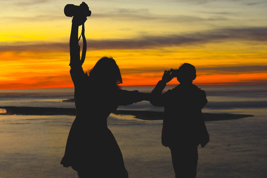 Silhouette of man taking pictures of woman at the beach at sunset during thier vacation
