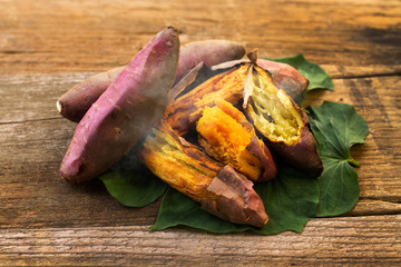 Delicious Roasted japanese sweet potato on wooden background with fresh green leaf.