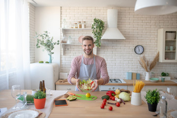 Smiling man holding bowl with salad after cooking