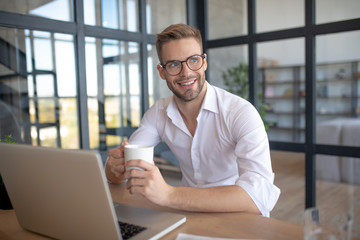 Blue-eyed businessman sitting near his laptop in the morning