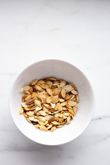 roast Pumpkin seeds in white bowl on marble background with copy space