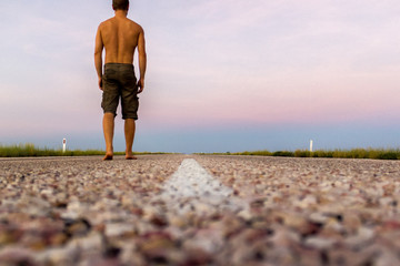 young man walking on straight road through the outback of Australia, after a beautiful sunset, Nothern territory