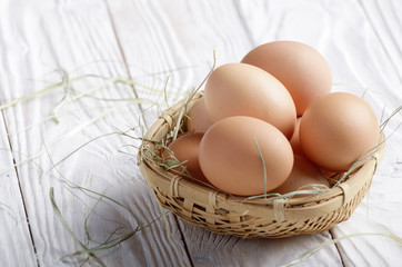 Raw organic brown chicken eggs in square wicker basket on white kitchen wooden table