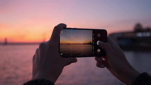Slow motion, the girl takes a photo on the phone of a beautiful and bright sunset in the sea, close-up.