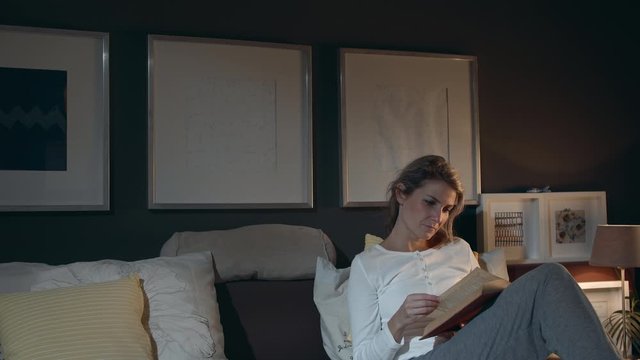 Wideshot of a young woman laying in bed while reading a book studying or engaged in a story. With space for text or animation