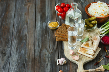 Vodka with lard, salted vegetables on wooden background. Alcohol pure craft drink and traditional snack, tomatos, cabbage, cucumbers. Negative space. Celebrating food and delicious.