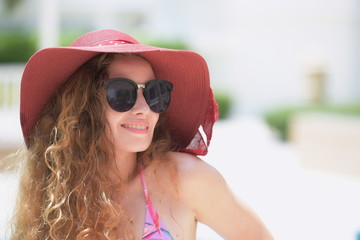 The woman in a swimsuit wears a hat and glasses at the poolside.