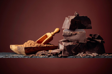 Black chocolate and wooden dish with cocoa powder on a brown background.
