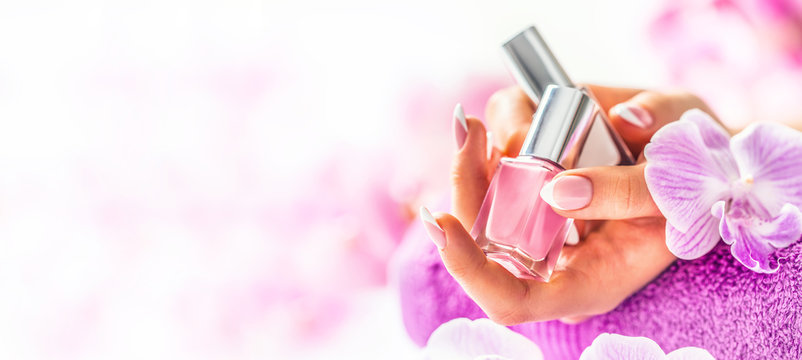 Trendy nail manicure. Woman hands holding nails polishes. Pink decoration from orchids