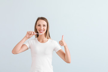 Portrait of woman brushing teeth on light background