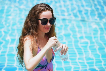 Beautiful girl in a bathing suit is drinking water from a bottle	