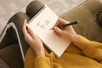 Woman making to-do list while sitting on sofa, closeup