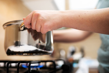 Beautiful young woman housewife prepairing dinner, hold in hands big steel saucepan, standing it on gas-stove.