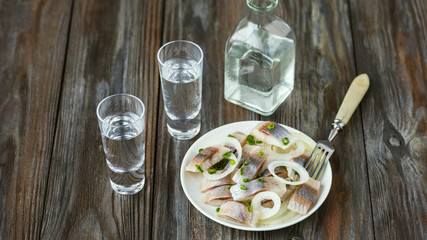 Vodka with salted herring and onion on wooden background. Alcohol pure craft drink and traditional snack. Negative space. Celebrating food and delicious.