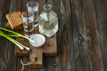 Vodka with green onion, bread toast and salt on wooden background. Alcohol pure craft drink and traditional snack. Negative space. Celebrating food and delicious.