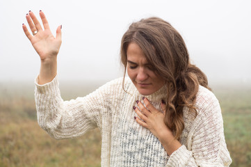 Girl closed her eyes, praying in a field during beautiful fog. Hands folded in prayer concept for...