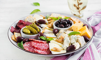 Fototapeta na wymiar Antipasto platter with basturma, salami, blue cheese, nuts, pickles and olives on a white wooden background.