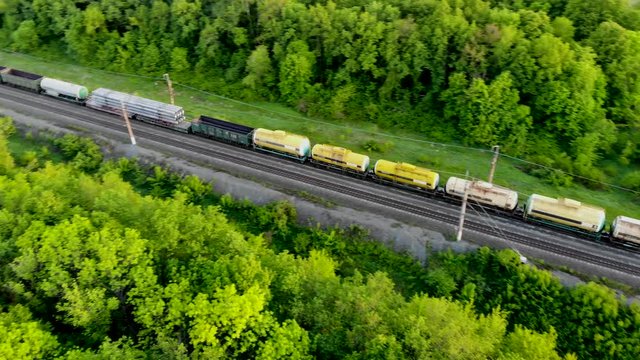 Aerial flying for freight train which delivers goods and containers through the countrys. The railway network is laid through forests and fields. Taken by drone at sunset