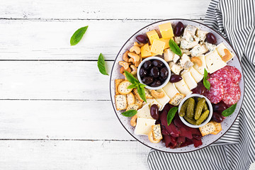 Antipasto platter with basturma, salami, blue cheese, nuts, pickles and olives on a white wooden background. Top view, overhead