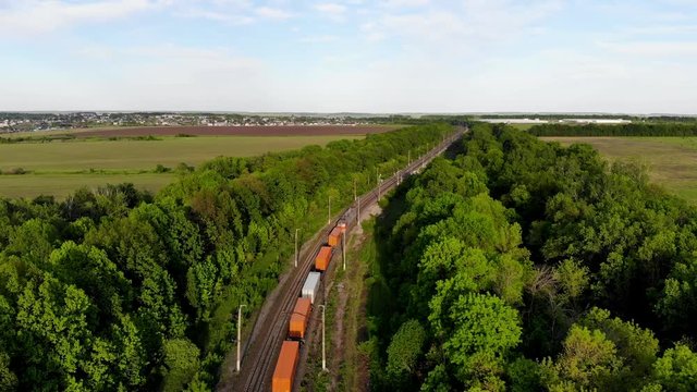 Aerial flying for freight train which delivers goods and containers through the countrys. The railway network is laid through forests and fields. Taken by drone at sunset